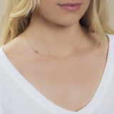 A close-up of a woman's neck wearing a 14k Gold Asymmetrical Number Necklace - 6 in yellow gold, styled with blonde hair and a white top.