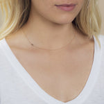 A close-up of a woman's neck wearing a 14k Gold Asymmetrical Number Necklace - 3 in yellow gold, styled with blonde hair and a white top.