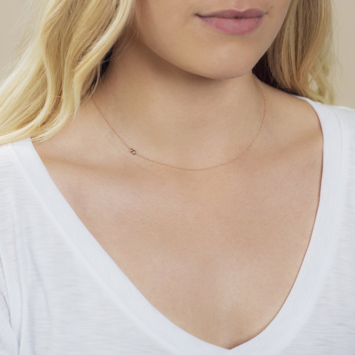 A close-up of a woman's neck wearing a 14k Gold Asymmetrical Number Necklace - 8 in yellow gold, styled with blonde hair and a white top.
