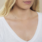 A close-up of a woman's neck wearing a 14k Gold Asymmetrical Number Necklace - 8 in yellow gold, styled with blonde hair and a white top.