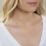 A close-up of a woman's neck wearing a 14k Gold Asymmetrical Number Necklace - 9 in yellow gold, styled with blonde hair and a white top.
