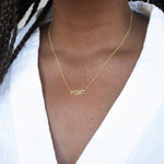 Close-up of a decellotage wearing a RiseUp Necklace with a white top. 