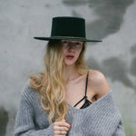 A woman wearing two yellow gold necklaces, one with a letter M charm, styled with a top hat and jumper.