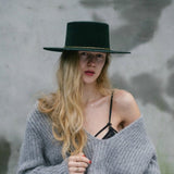 A woman wearing two yellow gold necklaces, one with a letter M charm, styled with a top hat and jumper.