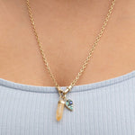 Close-up of a décolletage wearing an Oval Link Chain with an Abalone Leaf Charm and a Balance Crystal Charm with a light blue top. 
