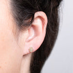 Close-up of an ear wearing a Pavé Charm Stud - Hamsa in yellow gold against a light grey background. 