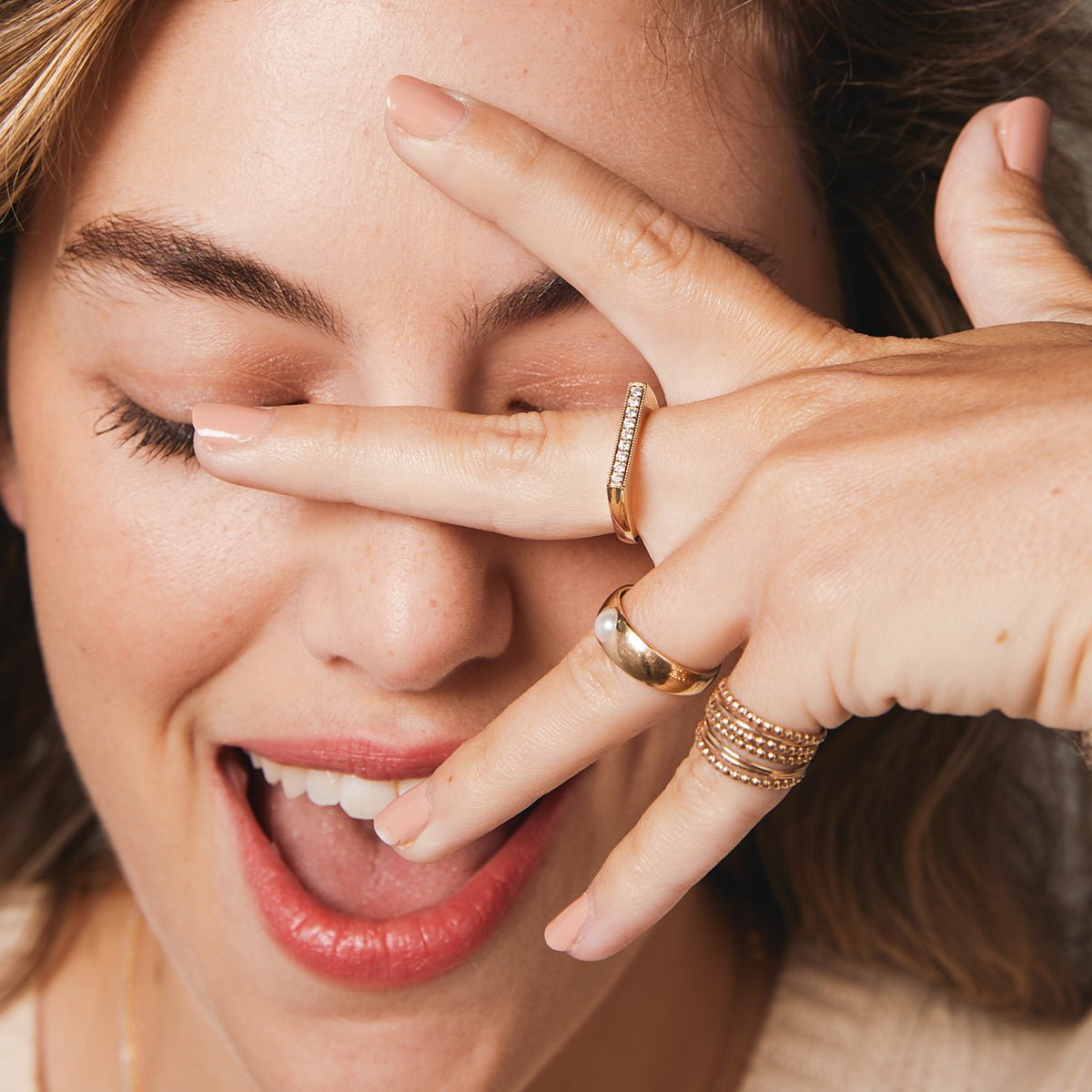 Close-up of a woman wearing a Perla Pinky Ring, Delicate Trio Stacking Rings and a Pave Geo Ring with her hand covering her face. 