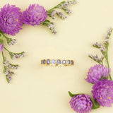 The Periwinkle Bouquet Ring on a light yellow background with purple flowers in two corners. 