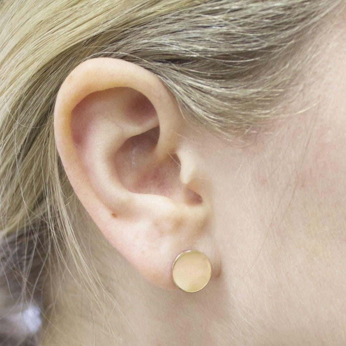 Close-up of a yellow gold Solid Eclipse Earring - Small in a blonde woman's ear. 
