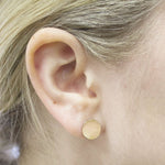 Close-up of a yellow gold Solid Eclipse Earring - Small in a blonde woman's ear. 
