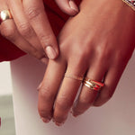 Close-up of hands wearing a Delicate Beaded Band, Delicate Twist Band, Thick Band, Geo Stacking Ring and two Tube Rings, all in yellow gold, against a light background. 
