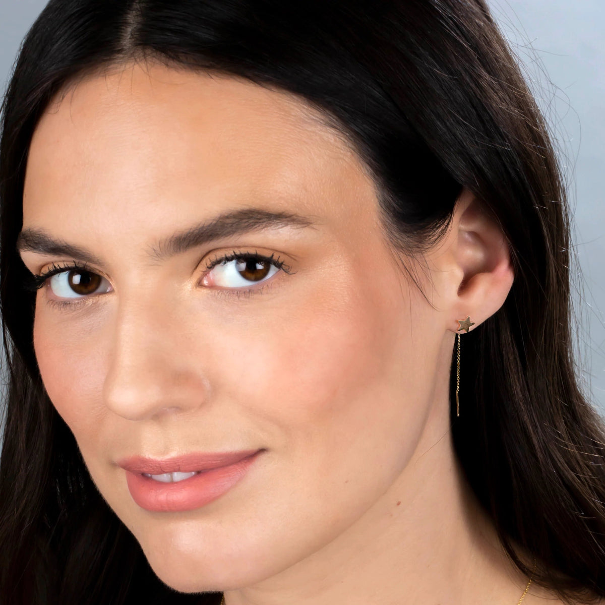 A 14K Gold Charm Threader Earring in star and yellow gold being worn by a brunette woman against a light grey background. 