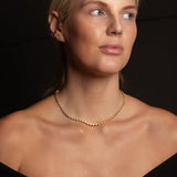 A blonde woman wearing The Ultimate Diamond Necklace in yellow gold with a black background. 