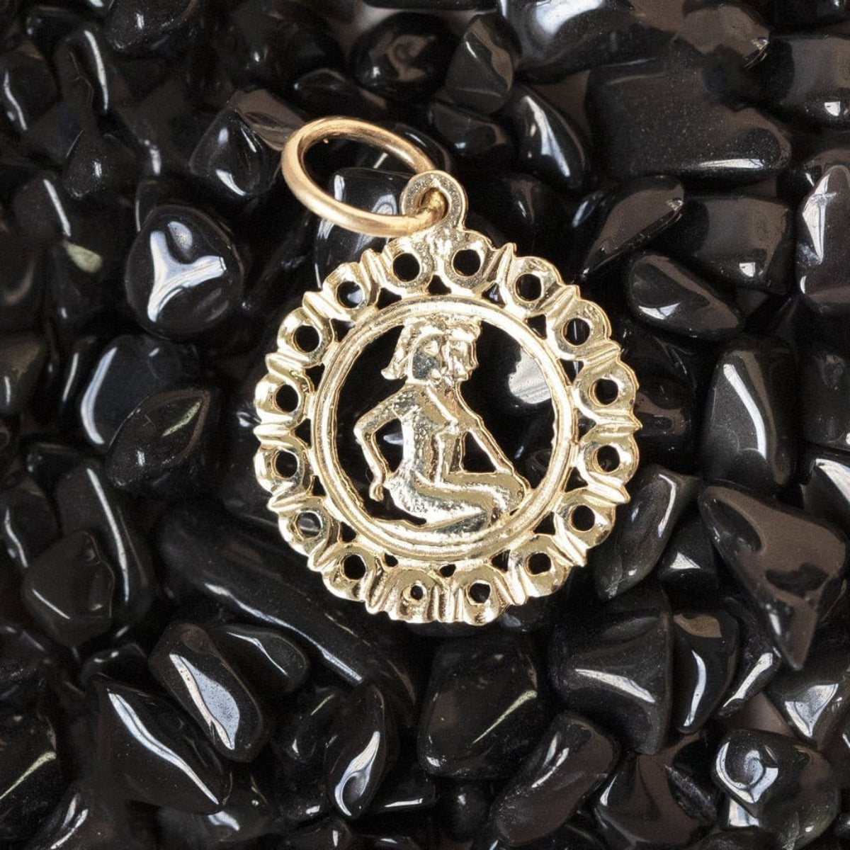 The Zodiac Necklace - Gemini pendant laid on top of black stones. 