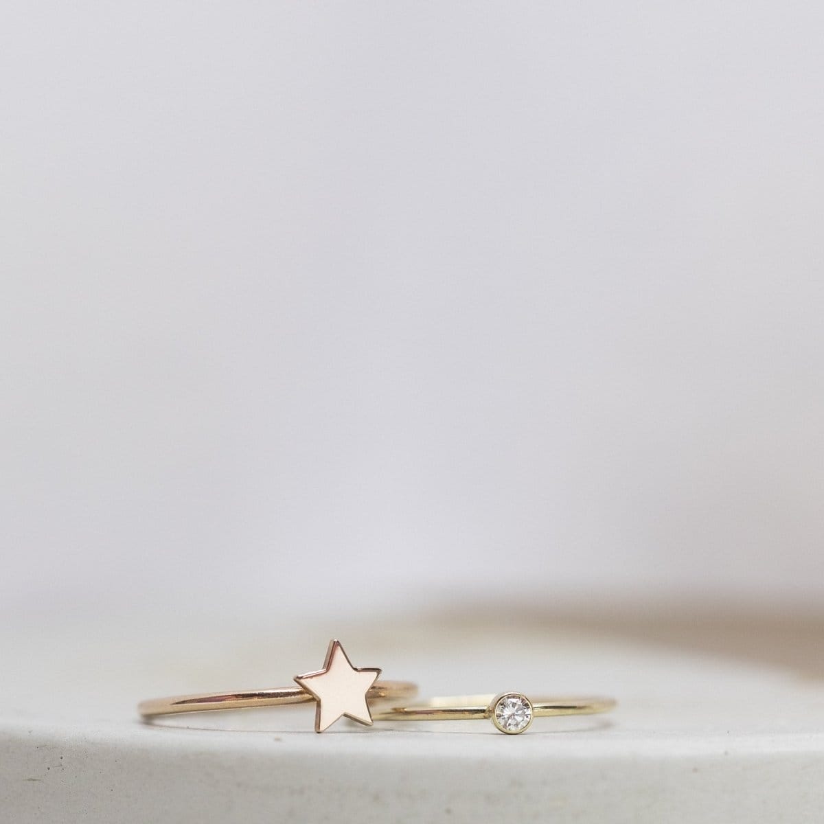 A rose gold Twinkle Twinkle Ring and yellow gold Birthstone Ring (Diamond) against a light grey blurred background.