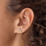 A close up of a woman's ear wearing a yellow gold pave diamond heart stud and a pave diamond moon stud.