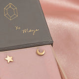 A yellow gold star charm stud and a yellow gold crescent moon stud in pink and grey box.