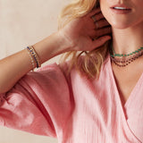 A woman wearing an assortment of bead chain necklaces and bracelets with a pink top on a neutral background