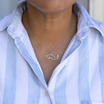 Close-up of a person's neck wearing a Mexico necklace in white gold with a blue and white striped shirt against a light grey blurred background.