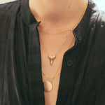 A close-up of a woman's neck wearing a black shirt and three rose gold necklaces: one with a letter P charm, one with a sharktooth with pavé on top, and one with a solid circle.