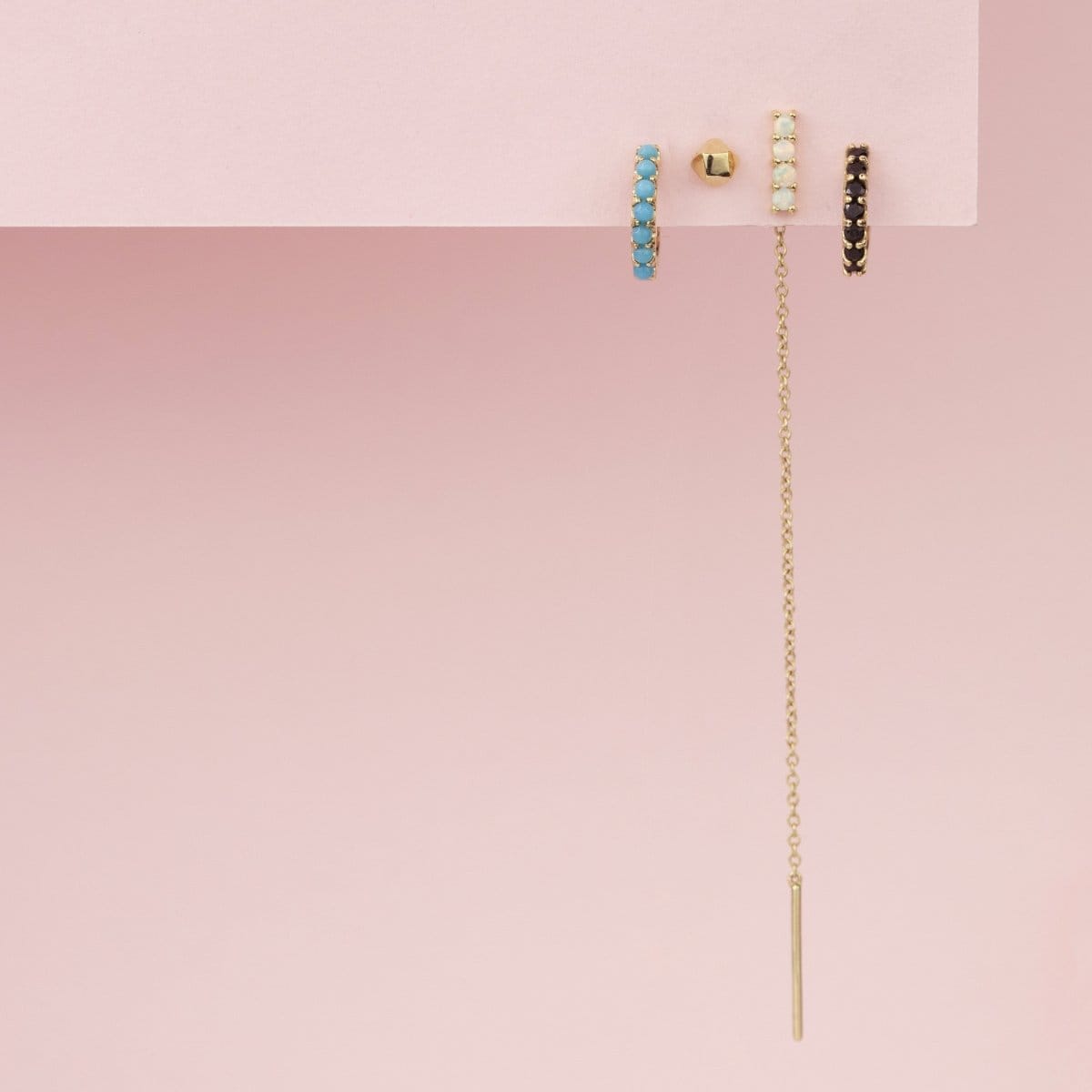 An Alli Webb Turquoise Huggie, Faceted Comfort Stud, Opal Threader and Onyx Huggie on a light pink background. 