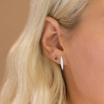 Close-up of a Birthstone Stud - Garnet (January) in white gold and a Horizon Stud in a blonde woman's ear against a light brown background. 