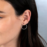 Close-up of a Rounded Ear Cuff, Birthstone Stud and a Circle Ear Jacket Pave in white gold in a brunette woman's ear against a light grey background. 