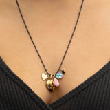 Close-up of a décolletage wearing a Black Rhodium Antique Bead Chain with the following charms - Engraved Heart Charm,  Diamond Heart Locket Charm, Pink Opal Tear Drop Charm, Small Abalone Cabochon Charm and a Onyx Dangle Charm  with a black top. 