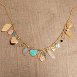 A Box Chain with the following charms - 
20th Anniversary Leaf Pendant, Pink Opal Tear Drop Charm, Turquoise Dangle Charm, Diamond Heart Locket Charm, Abalone Leaf Charm, Moonstone Crescent Charm, Turquoise Heart Charm, Large Abalone Cabochon Charm, two Balance Crystal Charms, Engraved Heart Charm, Small Abalone Cabochon Charm, Onyx Dangle Charm, Cut Out Heart Charm, Opal Dangle Charm and a Heart Locket Charm, against a beige fabric background. 