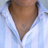 Close-up of a person's neck wearing a Brazil necklace with a blue and white striped shirt against a grey background. 