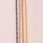 A Black Rhodium Antique Bead Chain, a Round Curb Chain, a Box Chain and a Oval Link Chain laid on an off-white fabric background.