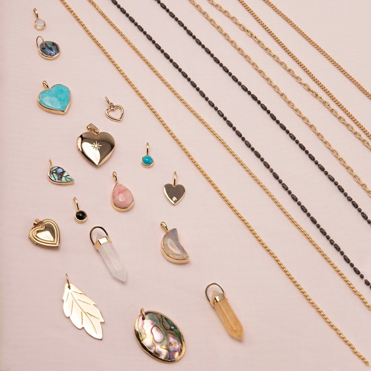 A Box Chain, Black Rhodium Antique Bead Chain, Oval Link Chain, Round Curb Chain,  Opal Dangle Charm, Small Abalone Cabochon Charm, Turquoise Heart Charm,
Cut Out Heart Charm, Diamond Heart Locket Charm, Abalone Leaf Charm, Turquoise Dangle Charm, Pink Opal Tear Drop Charm, Onyx Dangle Charm, Engraved Heart Charm, Heart Locket Charm, two Balance Crystal Charms, Moonstone Crescent Charm, 20th Anniversary Leaf Pendant and a Large Abalone Cabochon Charm against a light pink background. 