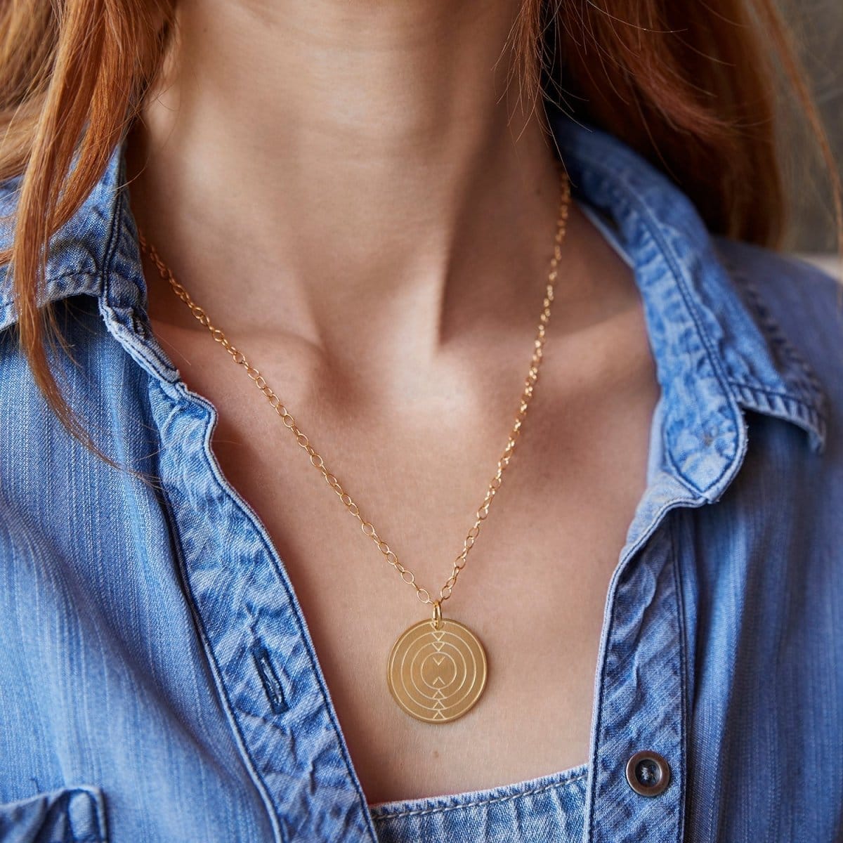 Close-up of a woman's neck wearing a Virtues Pendant - Circle in yellow gold with a blue denim shirt. 