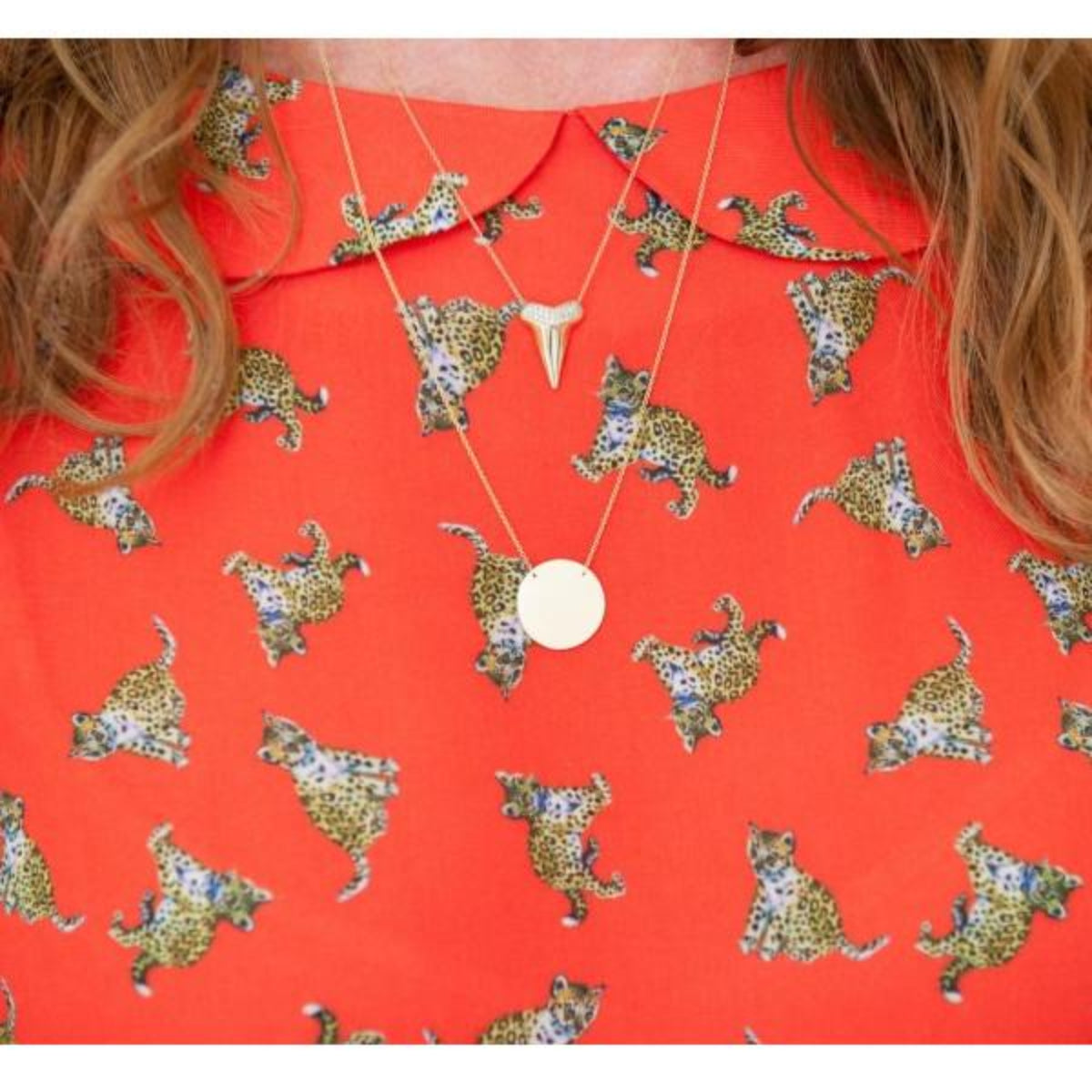 Close-up of a décolletage wearing a Sharktooth Necklace with Pavé Top and a Geometric Circle Necklace in yellow gold, with a red top featuring leopards. 