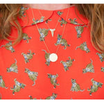 Close-up of a décolletage wearing a Sharktooth Necklace with Pavé Top and a Geometric Circle Necklace in yellow gold, with a red top featuring leopards. 