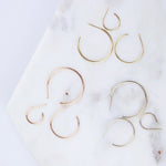 Crescent Hoops / Small, Medium and Large in rose, white and yellow gold on a white marble surface. 
