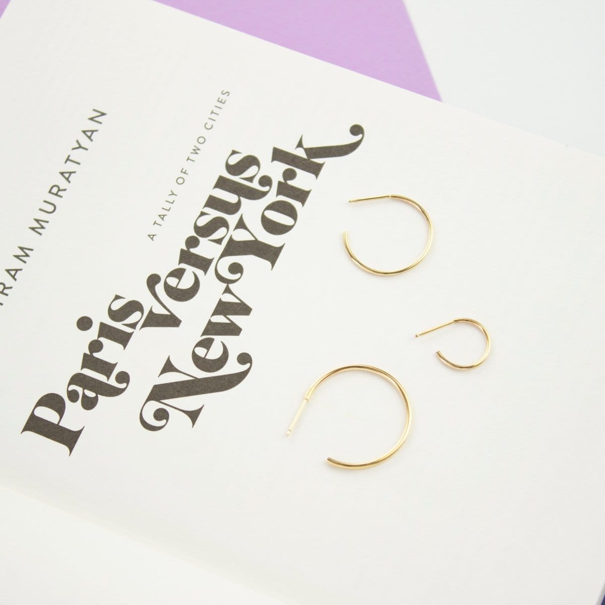 Three yellow gold Crescent Hoops in various sizes on a book titled 'Paris Versus New York'. 