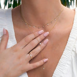 Close-up of a woman's décolletage wearing a Stardust Diamond Necklace, a Diamond Drip Necklace and a Tenfold Ring, styled in a white top with a leafy background. 