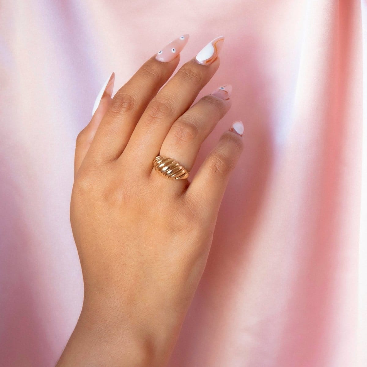 A hand wearing a yellow gold Etched Paris Ring against a pink and white blurred background. 