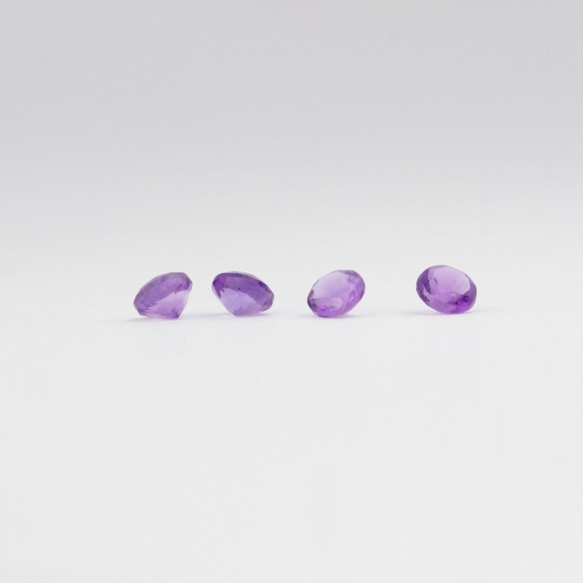 Four amethyst gemstones on a light grey background. 