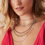 Close-up of a blonde woman wearing The Peony Bouquet Necklace, The Bluebell Bouquet Necklace, The Thistle Bouquet Necklace, The Closer Bouquet Necklace and The Sage Bouquet Necklace with a dark pink top against a neutral background. 