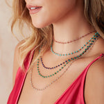 A close-up of a blonde woman's neck wearing Bouquet Necklaces (Peony, Bluebell, Thistle, Clover and Sage), with a dark pink strap top against a neutral background.  