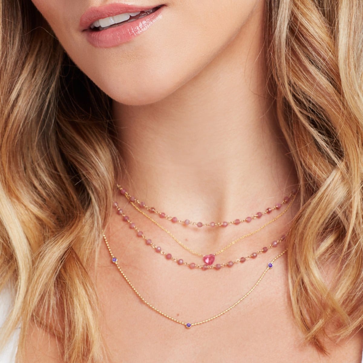 Close-up of a blonde woman's neck wearing a yellow gold Triple Birthstone Layering Necklace, The Sweetheart Necklace - Pink Sapphire and The Peony Bouquet Necklace. 