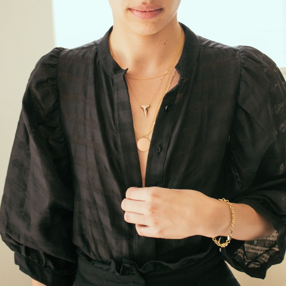 A woman wearing a 14K Gold Asymmetrical Letter Necklace - P, a Sharktooth Necklace with Pavé Top, a Geometric Circle Necklace, and a Rolo Bracelet, all in yellow gold, with a black shirt top against a light neutral background.