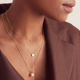 Close-up of a woman's neck wearing a yellow gold Diamond Layering Necklace, a Gold Lariat Necklace and a Perla Necklace, styled in a brown blazer. 