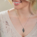 A blonde woman wearing the 20th Anniversary Leaf Pendant - Platinum, with a light beige knit and background.