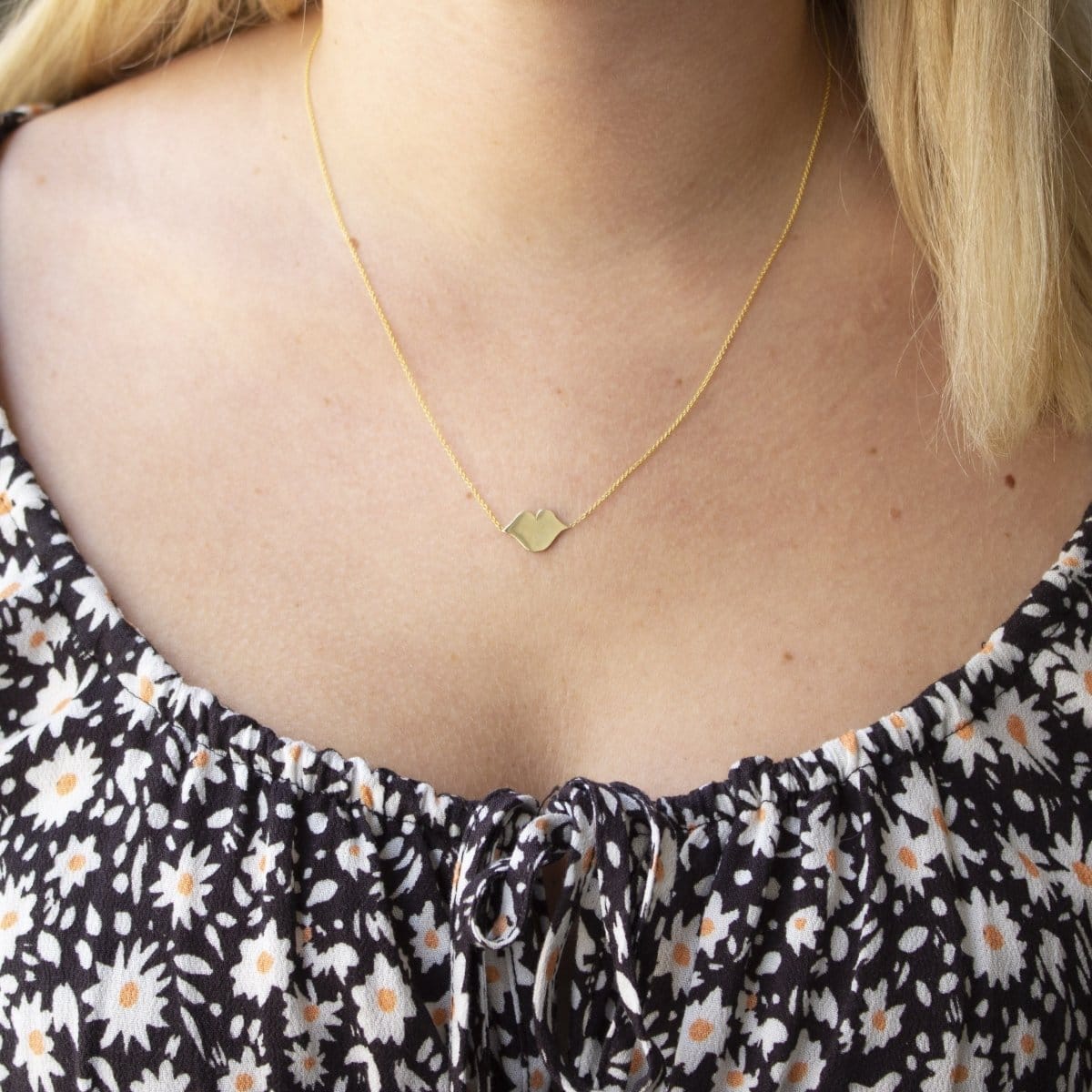 A blonde woman's décolletage wearing a  Lip Pendant necklace with a black top with white flowers. 