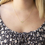 A blonde woman's décolletage wearing a  Lip Pendant necklace with a black top with white flowers. 