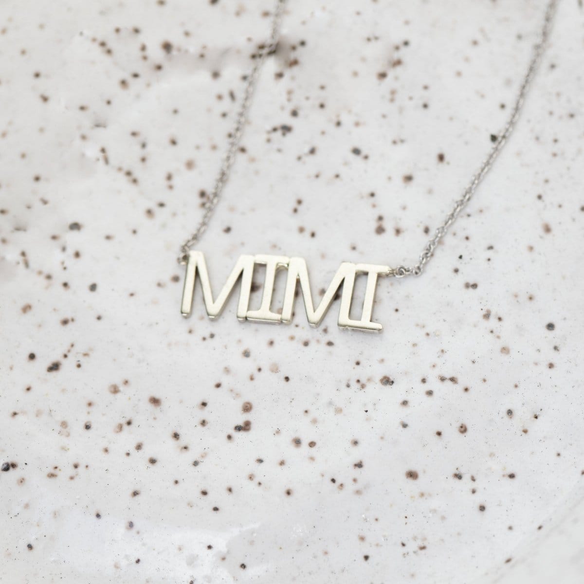 A MIMI Necklace in white gold with a cable chain on a speckled surface. 