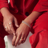 A close-up of a woman’s hands wearing several mixed metal bracelets - two Rolo Bracelets and three Diamond Cut Bracelets and yellow gold rings, a Thick Band, a Tres Pearl Ring, a Delicate Beaded Band, a Delicate Twist Band, a Geo Stacking Ring and two Tube Rings, in a red corduroy suit.